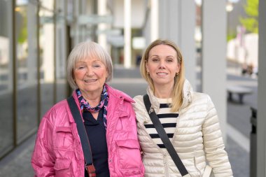 Anne ve kızı alışveriş merkezinde alışveriş yapıyor ve doğrudan kameraya bakıyor.