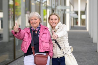 Anne ve kız alışveriş merkezinde alışveriş yaparken başparmak hareketi yapıyorlar.