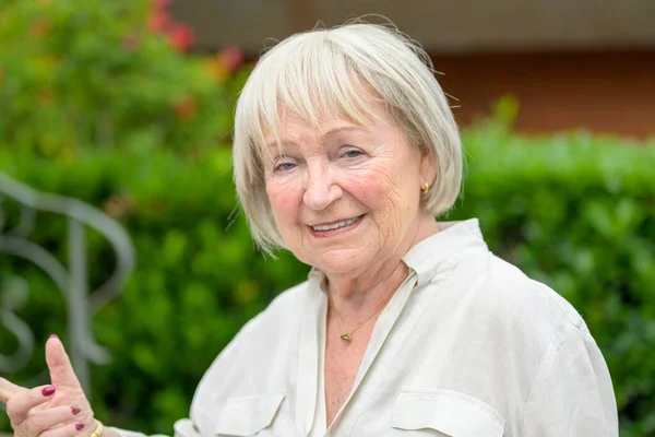 Oudere Vrouw Met Wit Haar Wijst Naar Zijkant Terwijl Glimlachend — Stockfoto