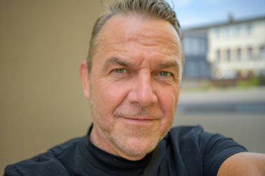 Çekici bir adam fotoğraf çekerken kameraya eleştirel bir şekilde bakıyor.