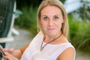 Kırklı yaşlarda genç ve çekici bir kadın kameraya bakıyor. Dostane bir gülümseme ve büyük gözlerle.