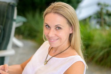 40 'lı yaşlarda çekici bir kadın terasta otururken psikopat bir sırıtışla yukarı bakıyor.