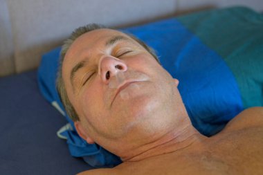 Close up of a sleeping middle aged man with a nose tape and a mouth tape lying in bed clipart