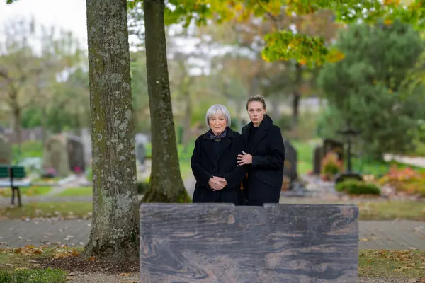 在阴冷的日子里 母亲和女儿站在墓地男人的墓前 看着摄像机 — 图库照片