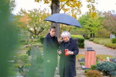 Anne ve gelini bulutlu bir günde oğlunun mezarında mum yakmaya çalışıyorlar.