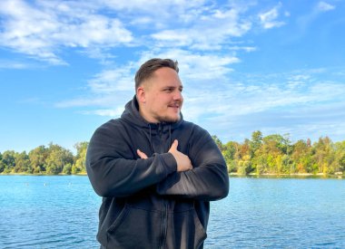 Genç adam sonbaharda kolları çaprazlanmış olarak gölün kıyısında duruyor.