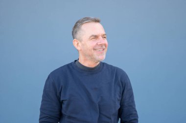 Orta yaşlı bir adamın üst vücut portresi. Uzağa bakıyor. Mavi bir süveter giymiş bir gülümsemeyle.