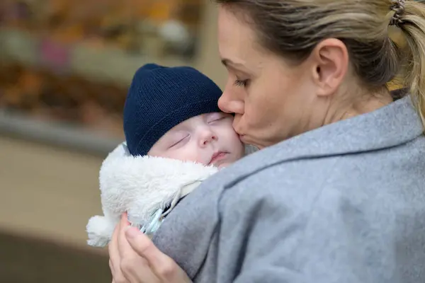 赤ちゃんのキャリアに彼女の新生児を保持し 愛情深い屋外にキス彼女の40代で幸せな母親の近くに — ストック写真