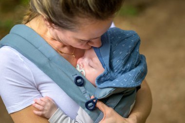 Bir bebeğin annesinin göğsünde ya da göğüs dekoltesinde uyuyan bir bebeğe aşırı derecede yakın, mavi bir şapka takarak.