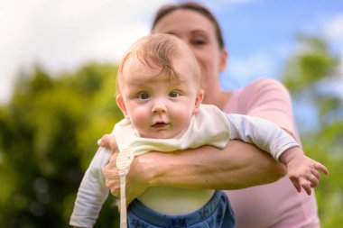 Bir anne bebeğini sevinçle kucağına alır ve bebek doğrudan kameraya bakar..