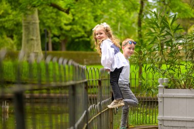 İki küçük çocuk, bir kız ve bir oğlan, parkta çitlere tırmanıyorlar..