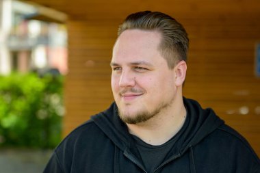 Kısa saçlı ve sakallı genç bir adam hafif bir gülümsemeyle yan tarafa bakıyor.