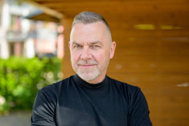 Kısa gri saçlı ve sakallı olgun bir adam düşünceli bir şekilde mesafeye bakar.