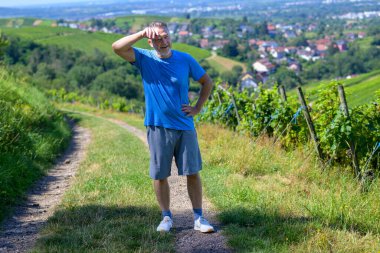 Üzüm bağı tepelerinde zorlu bir yürüyüşten sonra atletizm kıyafeti giyen bir adam mola verir..