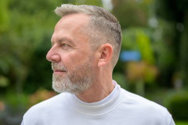 Beyaz gömlek giymiş, düzgün budanmış gri sakallı ve kısa saçlı olgun bir adamın yakın plan profili..