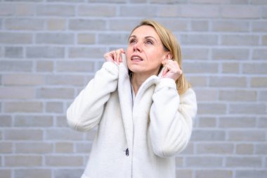 Beyaz önlük giymiş sarışın bir kadın düşünceli ve sakin bir ifadeyle yukarı bakıyor..