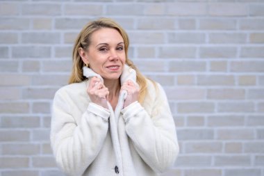 Nazikçe gülümseyerek yakasını tutan yumuşak beyaz ceketli sarışın bir kadın..