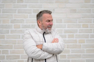 Gri sakallı ve açık renkli ceketli olgun bir adam kollarını kavuşturup dikkatlice yan tarafa bakıyor..