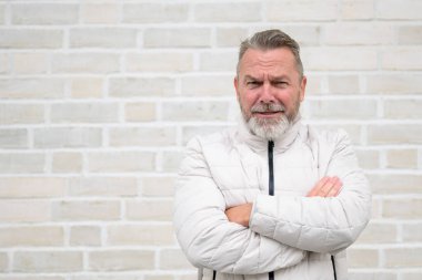 Gri sakallı, olgun bir adam kollarını kavuşturmuş, kurnaz bir gülümseme sergiliyor..