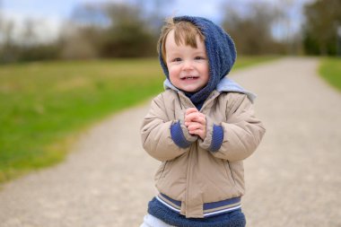 Çakıl yolu üzerinde bej renkli yorgan ve rahat mavi bir başlık giymiş genç bir çocuk sevinçle ışıldıyor..
