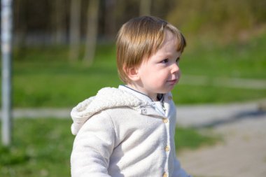 Genç bir çocuk dışarıda duruyor, yumuşak güneş ışığıyla yıkanmış, rahat krem rengi kapüşonlu bir kapüşon giyiyor..