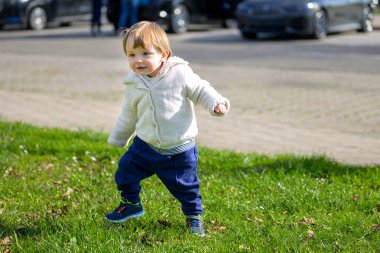 Neşeli bir çocuk, rahat bir kapüşonlu ve mavi pantolonlu, çimenli bir alanda güvenle yürüyor..