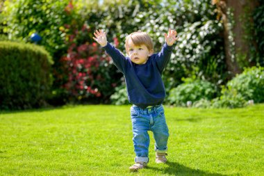 Neşeli bir çocuk, güneşten sırılsıklam olmuş bahçede yürürken iki kolunu da havaya kaldırır..