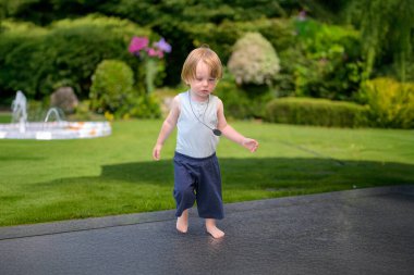 Genç bir çocuk yemyeşil bir bahçede, taştan bir terasta yalınayak yürüyor..