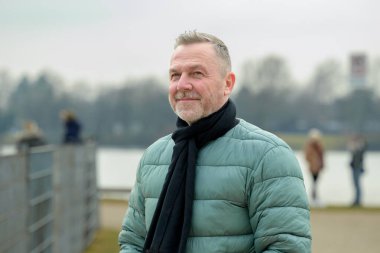 Yeşil yastıklı ceketli ve siyah eşarplı olgun bir adam sakince uzaklara bakar..