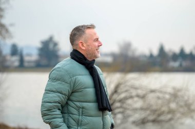 Nane yeşili kabarık ceketli ve siyah eşarplı gülümseyen bir adam gölün kenarında sakin bir anın tadını çıkarırken görüntülendi..