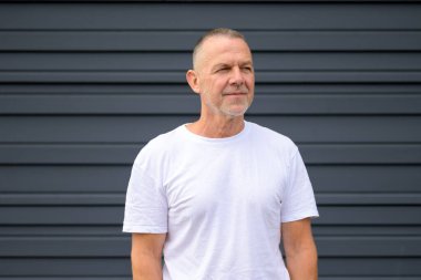 Beyaz tişörtlü kendinden emin son sınıf öğrencisi karanlık modern bir duvarın önünde dikiliyor..