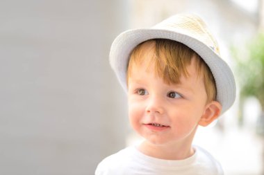 Hafif bir şapka ve beyaz tişört giyen gülümseyen bir çocuğun yakın çekimi..