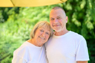 Güneşli yeşil bir bahçede kucaklaşan mutlu yaşlı bir çiftin portresi..