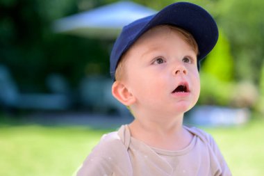 Mavi şapkalı genç bir çocuk meraklı ve şaşırmış bir ifadeyle dışarı bakar..