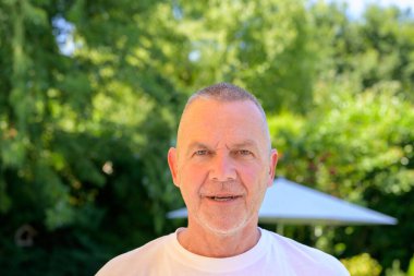 Gülümseyen bir kıdemli adam açık havada poz verir parlak bir yaz gününde.