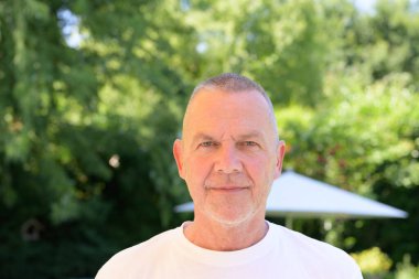 Ciddi bir kıdemli adam yazın açık havada çekilmiş bir portre boyunca ileriye bakar..