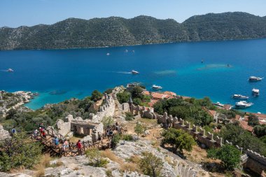 Kekova Körfezi 'nin göz kamaştırıcı manzarasını, masmavi suları, yemyeşil tepeleri ve Simena Kalesi' nin yıkıntıları arasında yer alan resmedilmiş Kaleky köyünü görüntüler..