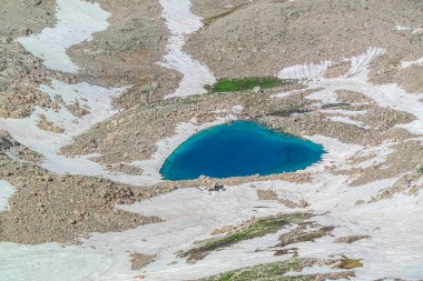 Engebeli bir dağ manzarasının ortasına kurulmuş çarpıcı alp kalbi şeklindeki göl.