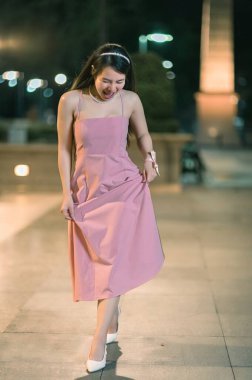 A joyful woman in a pink dress twirls gracefully on a stylish night out, showcasing her elegance and carefree spirit under the soft glow of evening lights. clipart