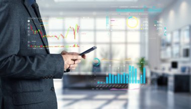 Bir işadamı dijital verileri ve grafikleri modern bir ofiste incelerken akıllı telefonunu kontrol eder. Bu resim, teknolojinin iş kararları ve analizlerine entegrasyonunu gösteriyor..