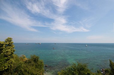Göz kamaştırıcı bir okyanus manzarası bulutlarla dolu açık mavi sularda tekneler gösteriyor. Bu dingin manzara huzuru ve doğanın güzelliğini yakalar..