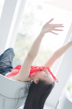 A joyful woman relaxes in a modern chair, arms raised in happiness. The bright indoor setting and her carefree expression embody a moment of leisure and serenity. clipart