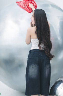 Uzun saçlı genç bir kadın kırmızı bir bez kullanarak büyük metalik bir küreyi zevkle temizliyor. Parlak iç mekan onun gündelik tarzını ve neşeli ruhunu vurguluyor..