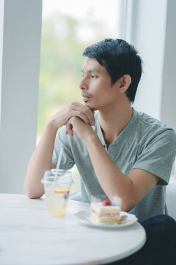 Düşünceli genç bir adam parlak bir kafede bir masada oturuyor, tatlı ve içkinin tadını çıkarıyor. Onun sakin tavrı ve sakin ifadesi sakin ve davetkar bir atmosfer yaratıyor..