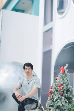 Genç bir adam güzel dekore edilmiş bir Noel ağacının yanında oturmuş modern dekorasyonla zarif bir iç mekanda şenlik ruhunu yakalıyor..