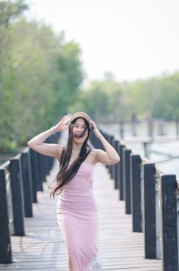 Genç bir kadın, yemyeşil yemyeşil, büyüleyici bir ahşap yolda neşe içinde poz veriyor. Gündelik elbisesi ve geniş gülüşü, doğada tasasız bir mutluluk hissi uyandırıyor..