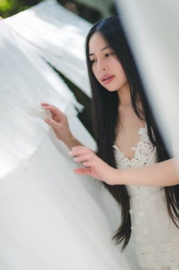 Beyaz elbiseli zarif bir kadının sakin portresi, açık havada güneşli bir günün tadını çıkarıyor, yumuşak kumaşların arasında, huzur ve güzellik saçıyor..