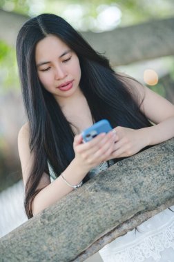 Genç bir kadın dışarıda duruyor, akıllı telefonuyla meşgul, ellerini dokulu bir yüzeye koyuyor, teknolojiyi ve doğayı bir anda somutlaştırıyor..