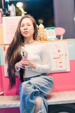 Genç bir insan elinde keyifli bir dondurma külahıyla, neşe saçan canlı bir şehir zeminiyle ve rahat bir yaşam tarzıyla rahatça oturur..