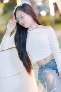 Genç bir kadın sıradan bir açık hava ortamında zarif bir şekilde poz veriyor. Rahatlamış güzelliği ve şık çekiciliği somutlaştırıyor, sakin bir atmosferde anın tadını çıkarıyor..